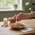 Asia Trade bitter apricot kernels in a ceramic bowl on a wooden table with a hand picking one kernel