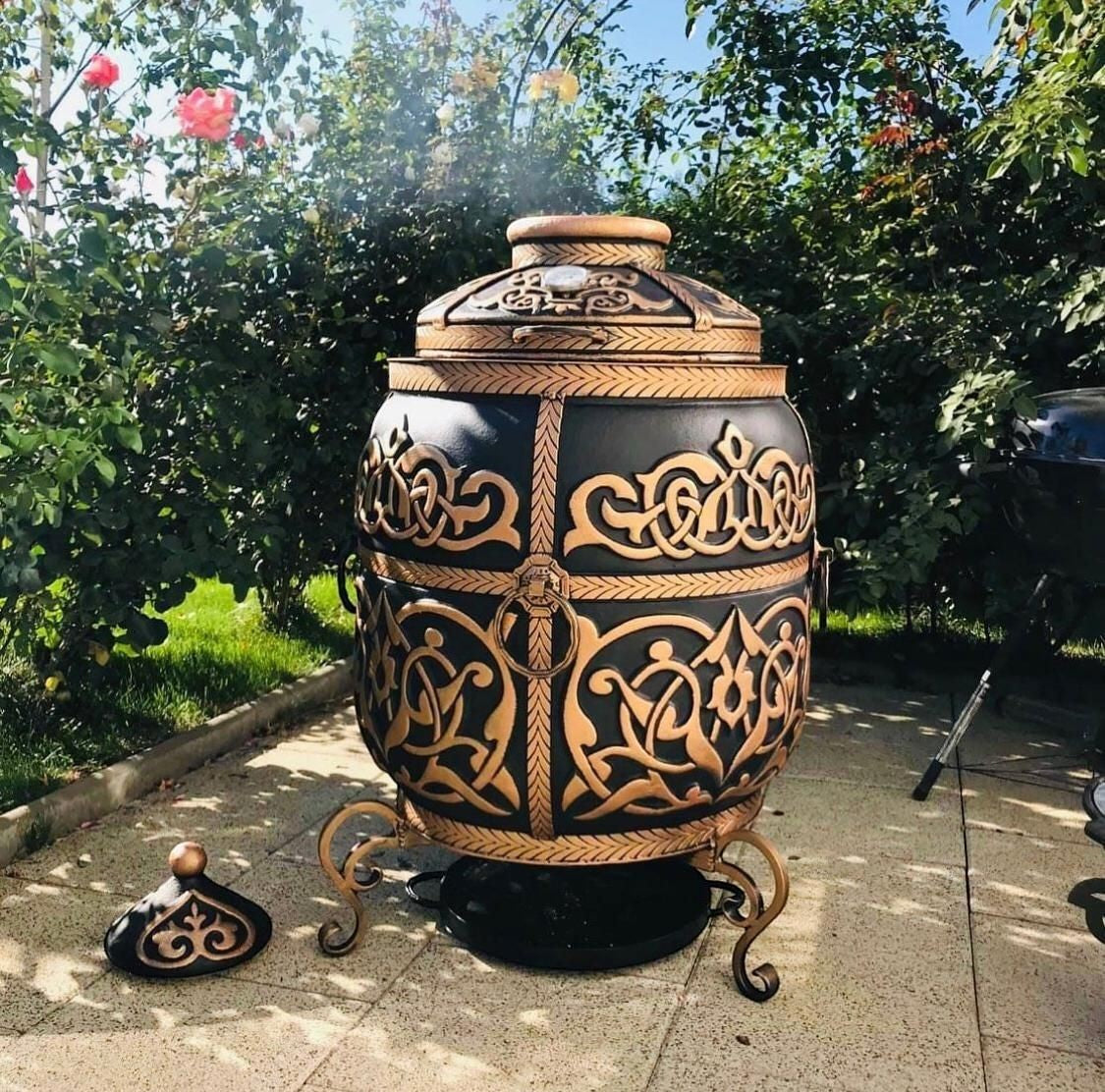 Asia Trade 100L insulated clay tandoor oven in black with ornate gold carved patterns, standing on decorative metal legs.