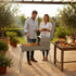 Asia Trade Kukmara black metal combination grill and stove with chimney, used by a couple in a sunny garden setting.