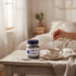 Asia Trade lavender herbal tea in a glass jar next to a steaming cup of tea with a sprig of lavender on a wooden table