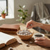 Asia Trade roasted apricot kernels with salt in a wooden bowl on a wooden table with a cup of coffee and a book